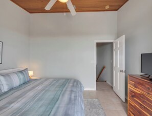 A bedroom with a bed, a TV, a wooden dresser, and a ceiling fan. - Southern Sunshine, Beachfront Living — Fully Updated & Steps to the Sand (Navarre Beach)