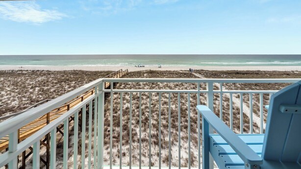 Une vue sur la plage depuis une terrasse couverte, dotée d’une rambarde en bois et d’une chaise bleue.