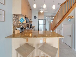 A kitchen with a central island, a wooden staircase, and a ceiling fan. - Southern Sunshine, Beachfront Living — Fully Updated & Steps to the Sand (Navarre Beach)