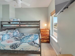 A bunk bed with patterned bedding, a bedside table with a lamp, and a window with a view. - Southern Sunshine, Beachfront Living — Fully Updated & Steps to the Sand (Navarre Beach)