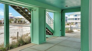 Un bâtiment à l’extérieur verdoyant, avec un escalier menant à un deuxième étage, et offrant une vue sur une plage et d’autres bâtiments.