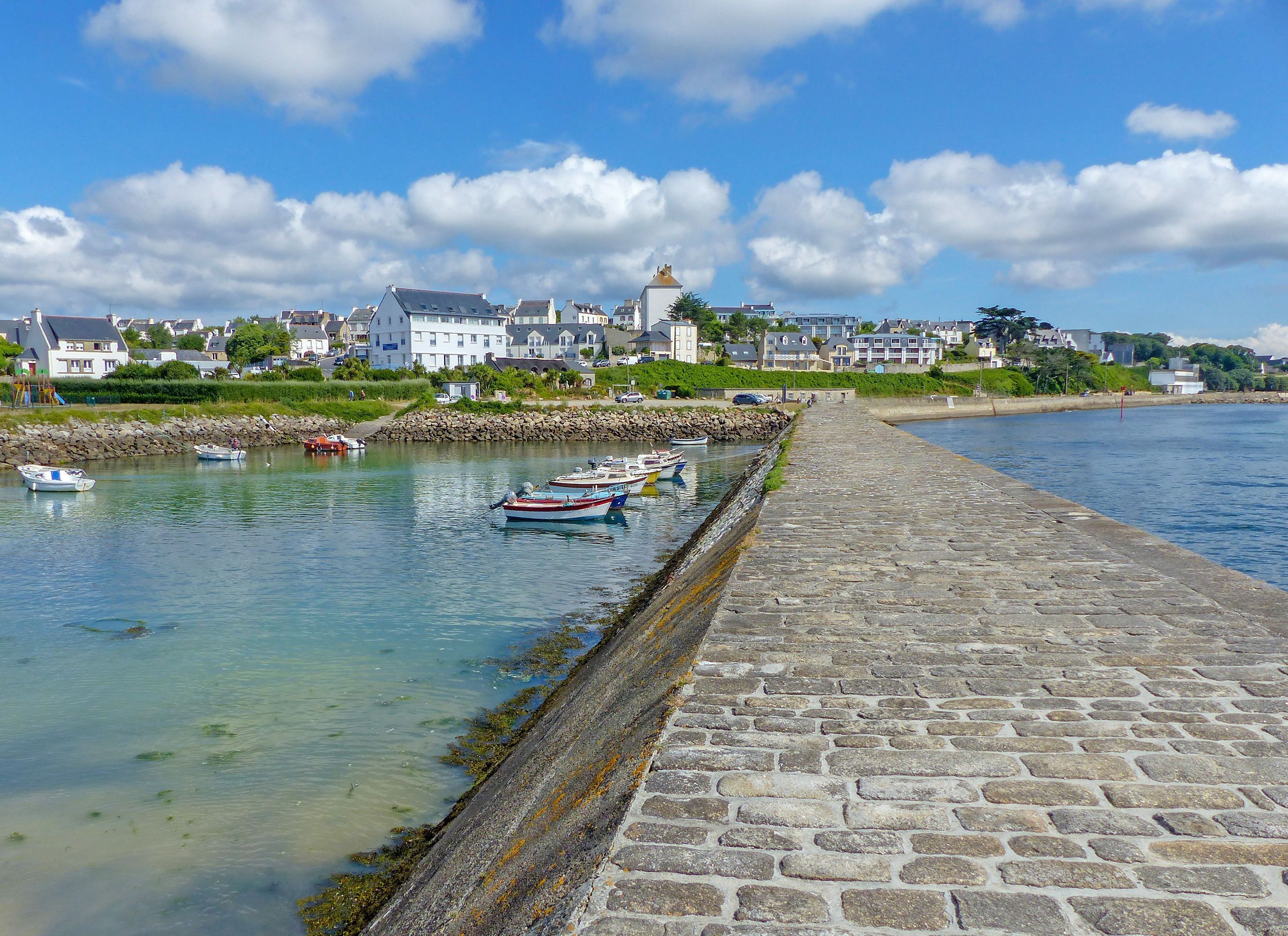 A waterfront scene with boats docked, a stone quay, and buildings in the background.