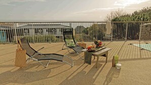 Terraço no telhado com duas cadeiras de estar, uma mesa com uma cesta de frutas e vista para edifícios ao fundo.