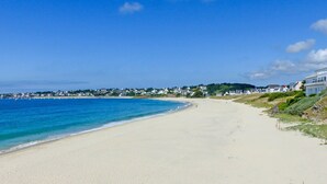 Une plage avec un ciel bleu dégagé, un rivage sablonneux et des maisons qui bordent la côte.