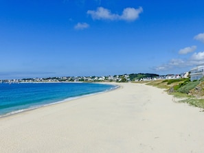 A beach with a clear blue sky, sandy shore, and houses along the coastline.