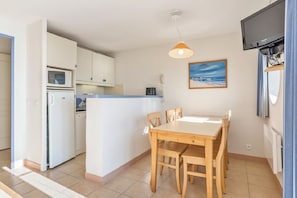 A compact kitchen with a dining area, a microwave, a kettle, a small island, and a TV mounted on the wall.