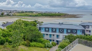 A coastal hotel with a view of the beach and sea, featuring a blue and white facade, a balcony, and a garden area. - Cosy T2 avec vue sur la ver | La plage à proximité (Audierne)