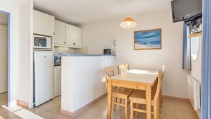 A compact kitchen with a dining area, a microwave, a kettle, a small island, and a TV mounted on the wall. - Cosy T2 avec vue sur la ver | La plage à proximité (Audierne)