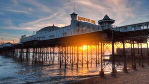 Un muelle con un faro y un edificio que dice 'Brighton Pier' bajo un cielo al atardecer.