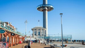 Un paseo marítimo con una torre alta, una galería techada y un edificio con ventanales arqueados.