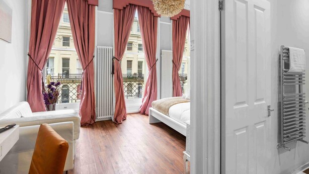 Et hotelværelse med seng, siddeplads, radiator og udsigt ud.