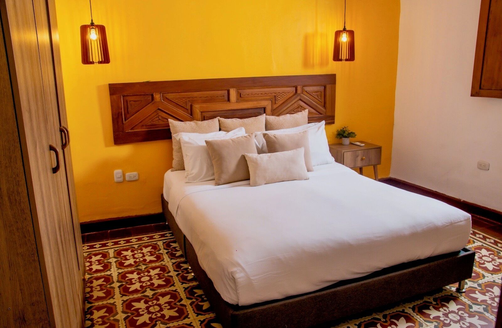 Una cama con cabecera de madera, un tapete estampado y dos lámparas colgantes.