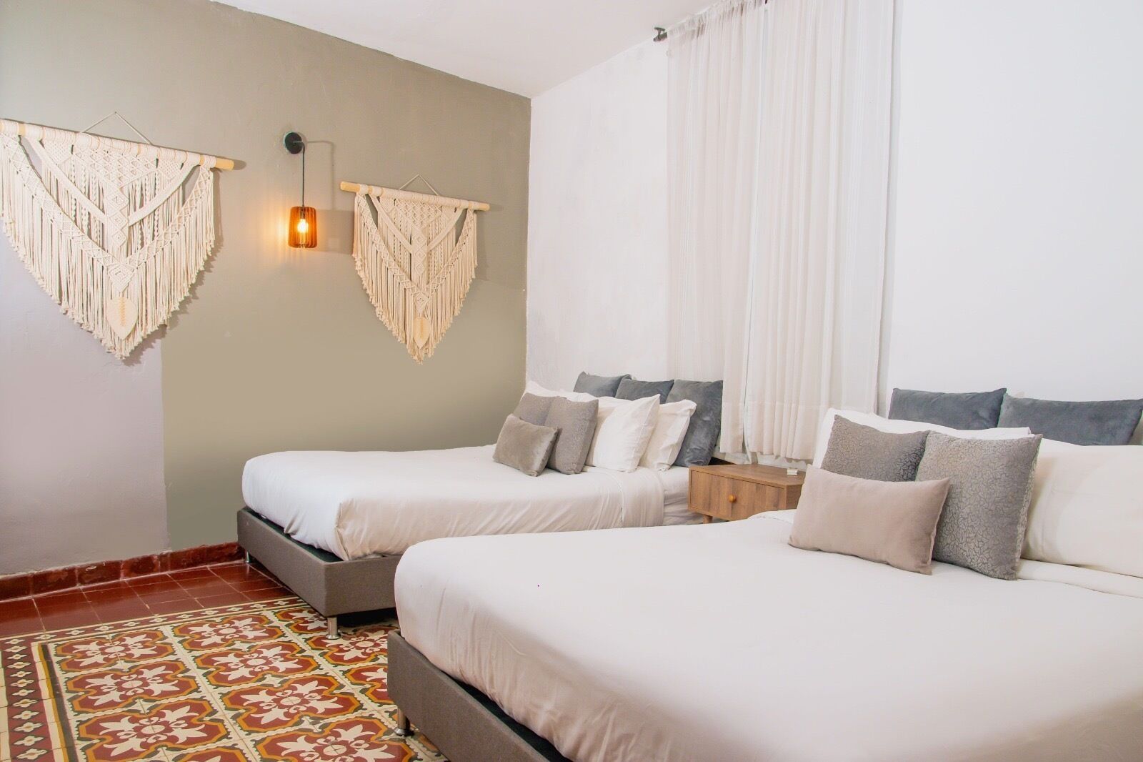 A hotel room with two beds, a patterned floor, macramé wall decorations, and a bedside lamp.