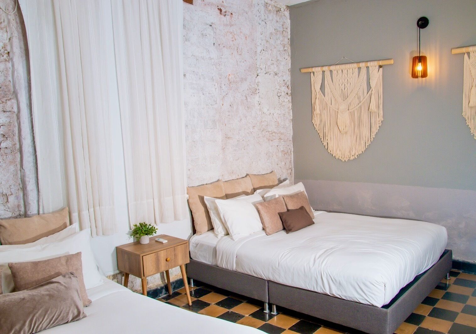 A bedroom with a large bed, a bedside table with a plant, a wall-mounted macrame decoration, and a textured wall.