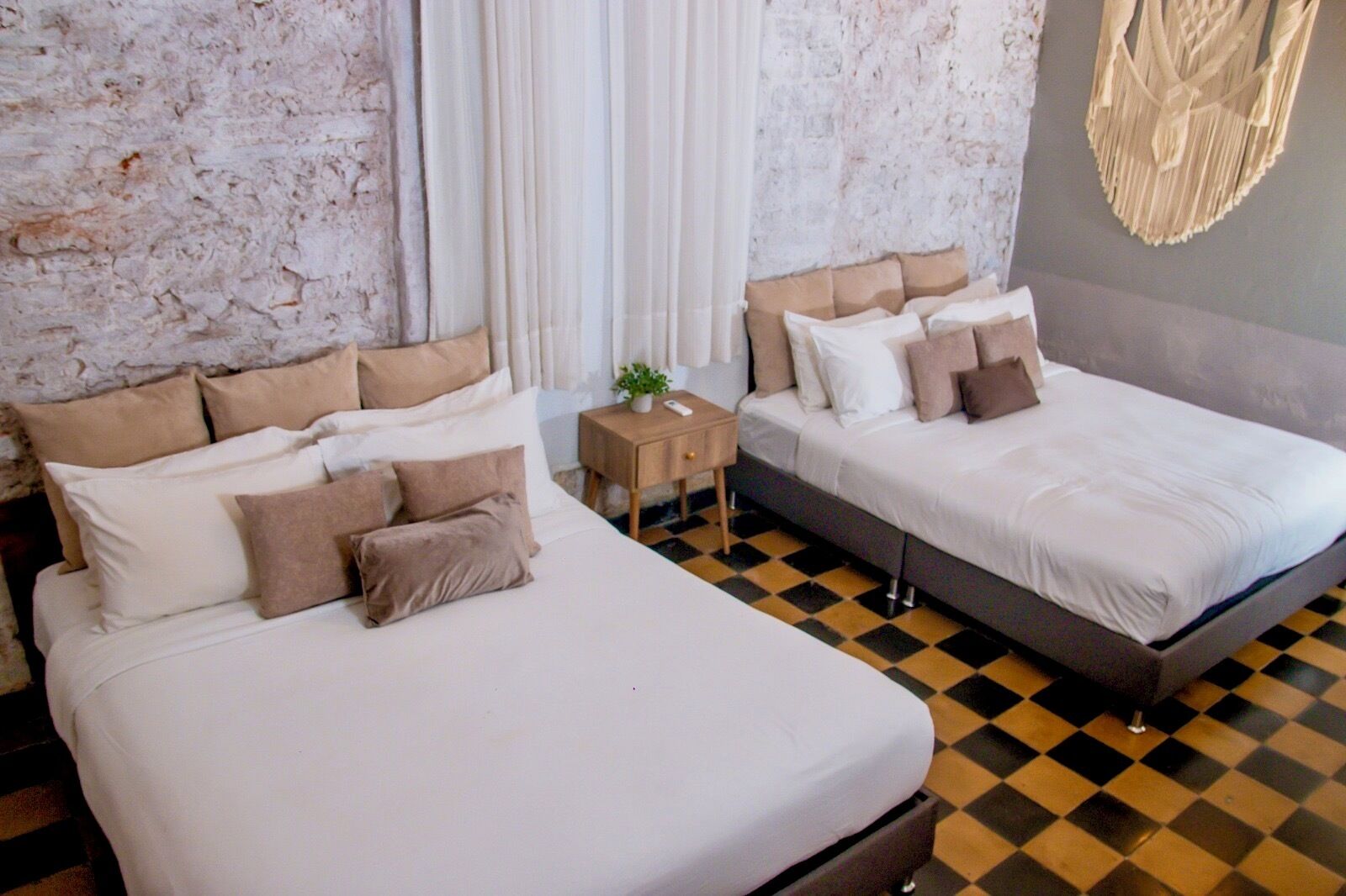 Quarto de hotel com duas camas, piso xadrez e parede texturizada.