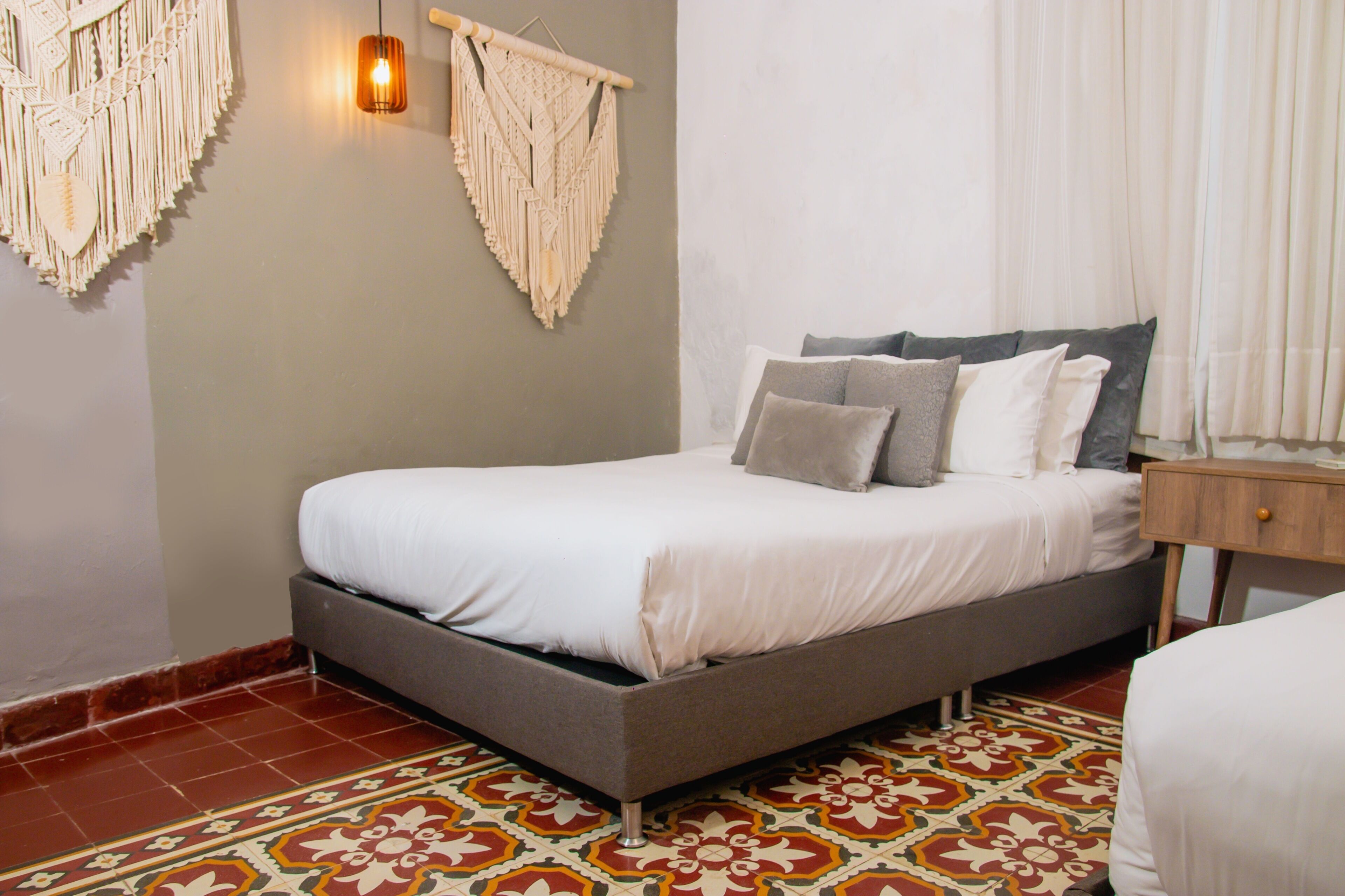 Een slaapkamer met een bed, een nachtkastje, een macramé decoratie aan de muur en een vloer met een patroon.