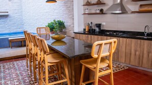 Une cuisine dotée d’un îlot central, de chaises en bois, de luminaires suspendus, d’une plante en pot et d’un pare-feu en carreaux.