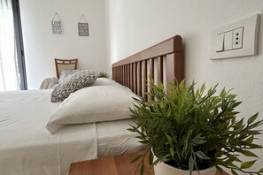 Ein ordentlich bezogenes Bett mit Holz-Kopfteil, einem Blumentopf und zwei Wandbildern.