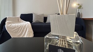 Un salon avec un canapé foncé, des coussins à motifs, un plaid blanc et un vase contenant de longues tiges fines.