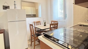 Une cuisine moderne avec une table à manger au plateau en verre, des chaises en bois, un réfrigérateur blanc et une fenêtre laissant entrer la lumière naturelle.