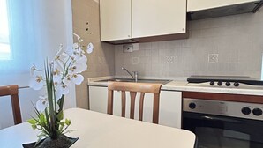 Une cuisine avec des meubles blancs, une cuisinière, un four, un évier et une table avec des chaises.
