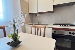 Eine Küche mit weißen Schränken, einem Herd, einem Backofen, einer Spüle und einem Tisch mit Stühlen.