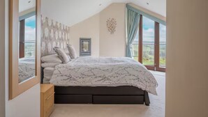 Ein Schlafzimmer mit einem großen Bett, einem Spiegel, einem Fenster und Blick ins Freie.