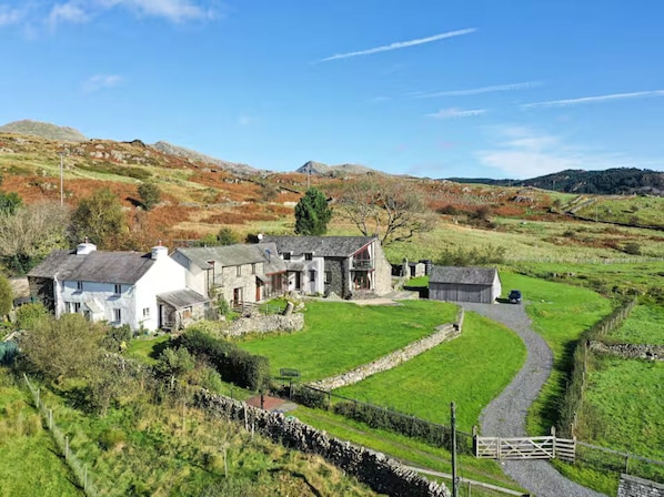 A rural house with a stone exterior, a gravel driveway, and a stone wall.