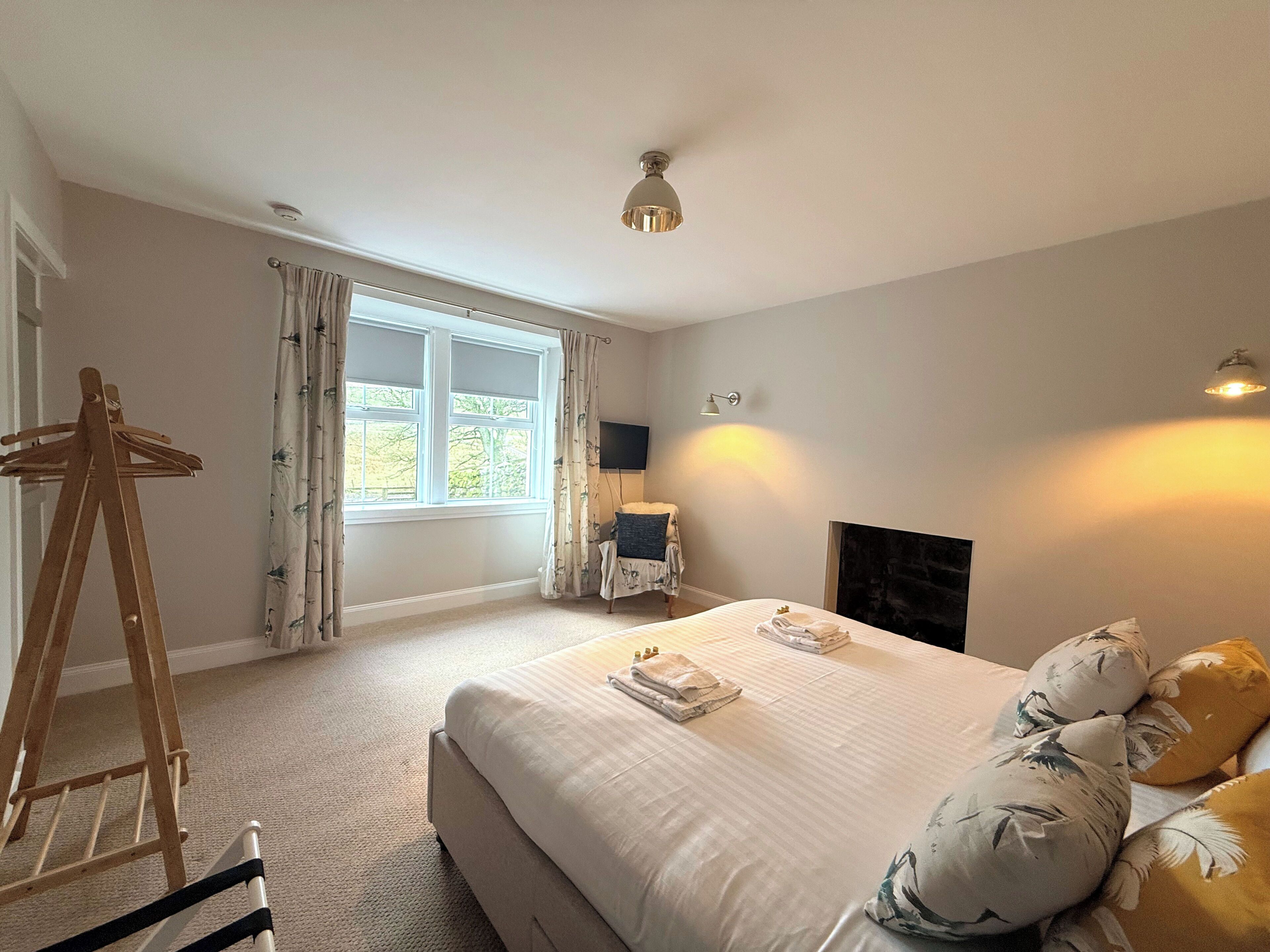 Een slaapkamer met een bed, een houten schildersezel, een raam met gordijnen, een wandlamp en een open haard.
