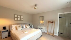 A bedroom with a large bed, bedside tables, a radiator, a mirror, and a clothing rack. - Luxury Scottish Cottage with Hot Tub & Views - Pass the Keys (Sanquhar)