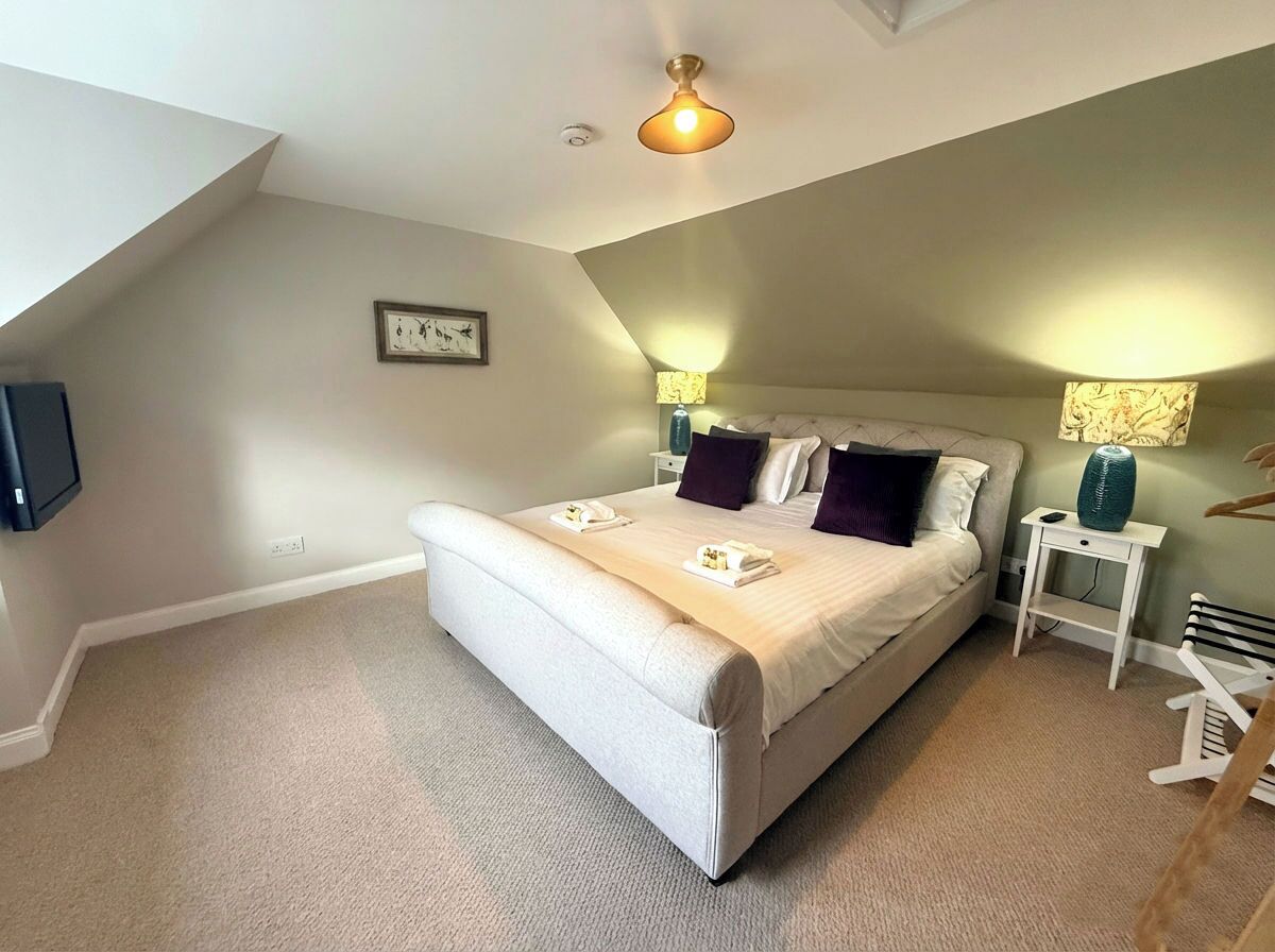 A bedroom with a large bed, two bedside tables, a ceiling fan, and a wall-mounted TV.