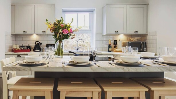 A modern kitchen with white cabinets, a marble countertop, and a central island with seating. - Luxury Scottish Cottage with Hot Tub & Views - Pass the Keys (Sanquhar)