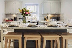 A modern kitchen with white cabinets, a marble countertop, and a central island with seating. - Luxury Scottish Cottage with Hot Tub & Views - Pass the Keys (Sanquhar)