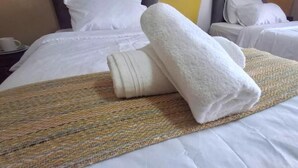 A hotel room with a neatly made bed, a woven blanket, and a rolled-up towel. - Neema Lodge (Boksburg)
