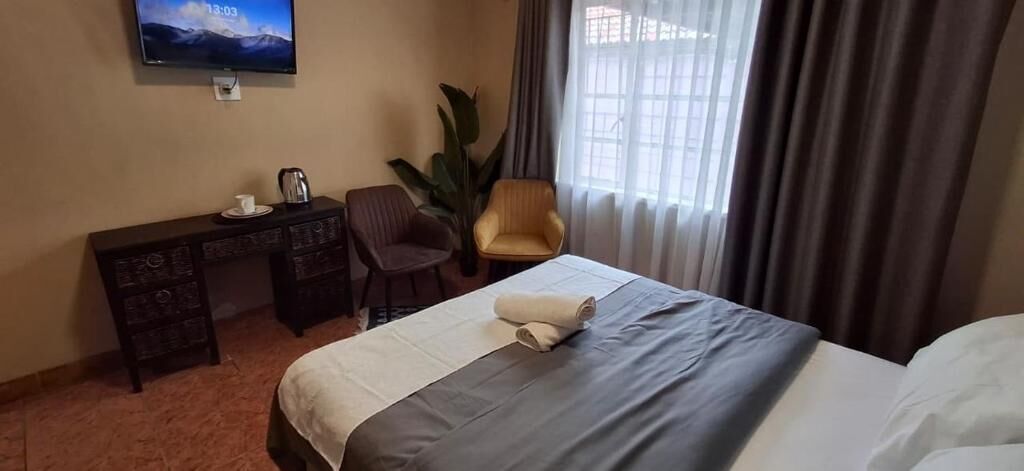 Una habitación de hotel con cama, escritorio, silla, televisor y una ventana grande con cortinas.