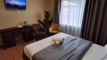 Ein Hotelzimmer mit Bett, Schreibtisch, Stuhl, Fernseher und einem großen Fenster mit Vorhängen.