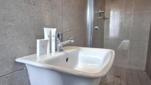 A bathroom with a white sink, a shower, and a tiled floor. - Neema Lodge (Boksburg)