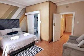 A hotel room with a bed, a chair, a wardrobe, and a door leading to another room. - Neema Lodge (Boksburg)