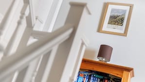 Un escalier avec des rampes blanches, un tableau encadré au mur et une bibliothèque remplie de livres.