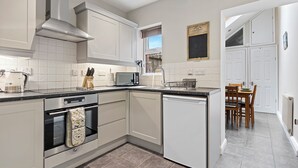 Une cuisine moderne avec des meubles blancs, un four encastré, un lave-vaisselle et un coin repas comprenant une table et des chaises.