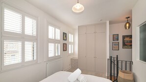 Ein Schlafzimmer mit Bett, Schrank, Heizkörper, einem Fenster mit Jalousien und einer Pendelleuchte.