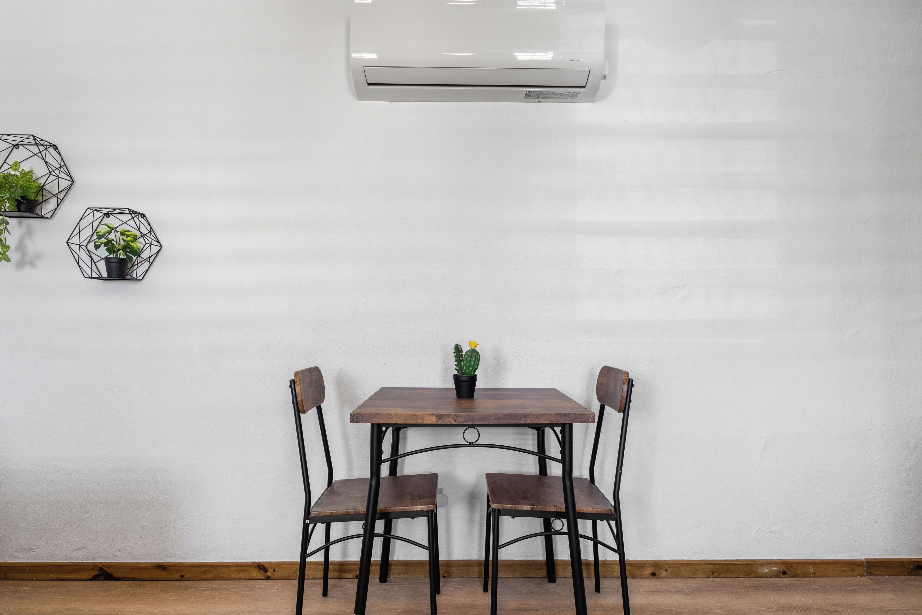 A room with a wooden table and chairs, an air conditioner, and hexagonal wall decorations with plants.