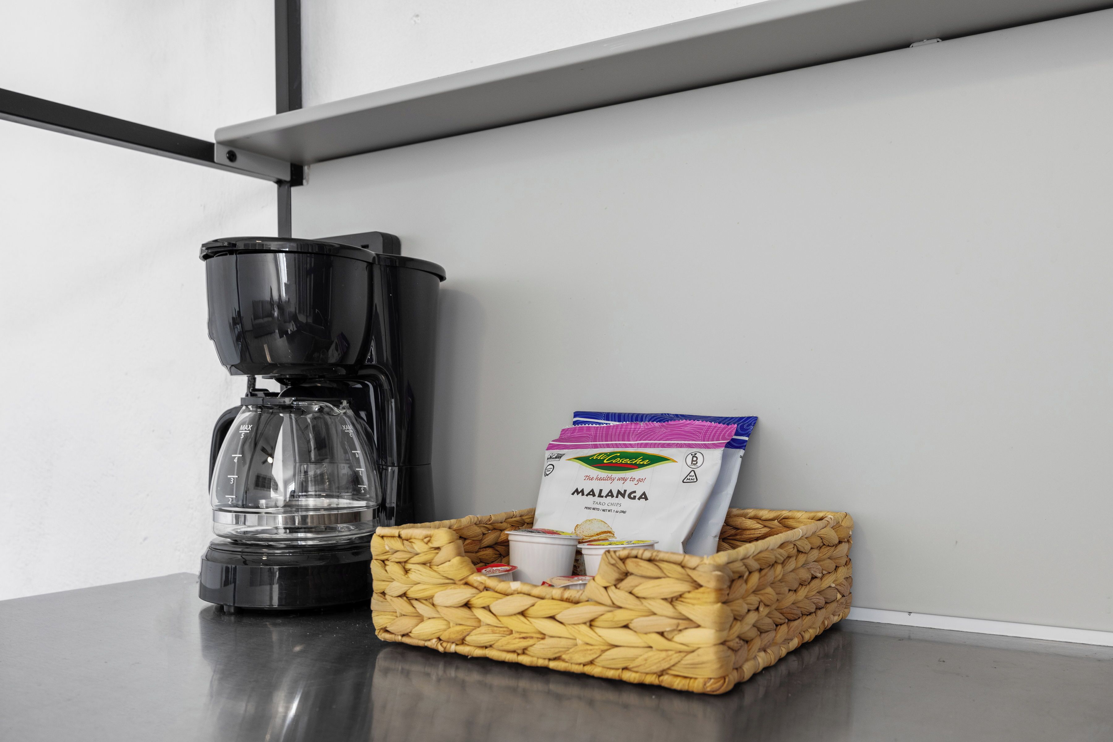 Une machine à café, un panier contenant un sac de patates douces et une tasse sur une table.