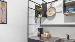 Een keuken met een RVS spoelbak, een hangplant, een koffiezetapparaat en een houten snijplank.
