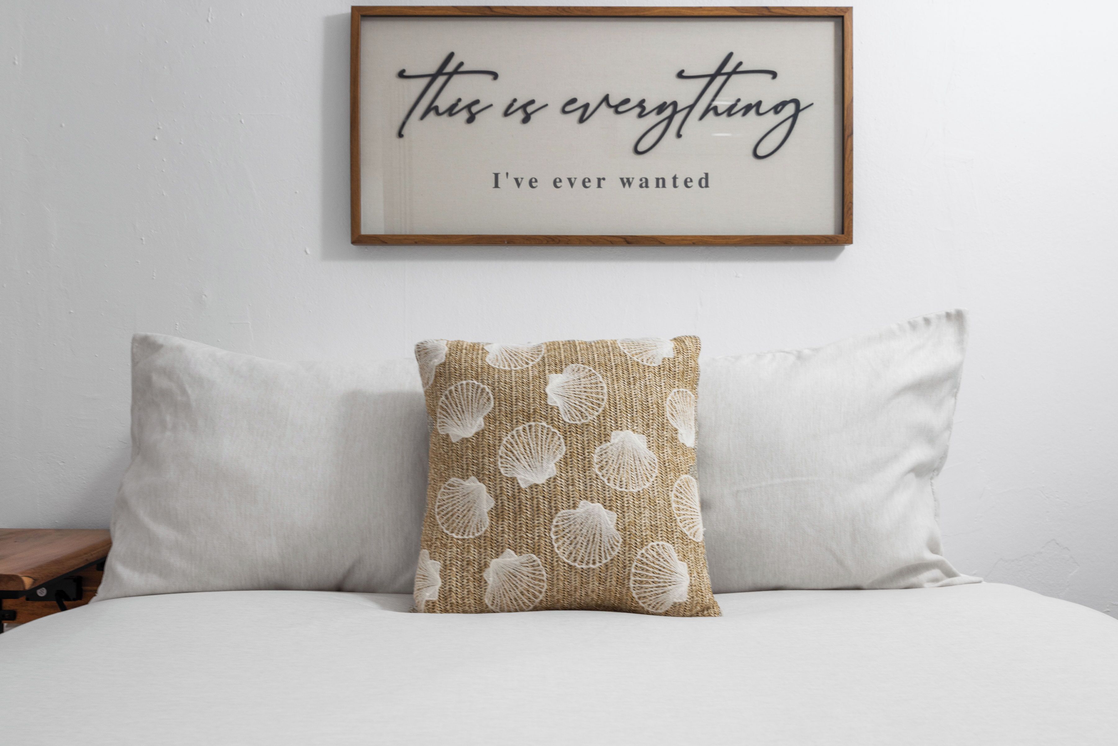 A bed with two pillows and a framed quote on the wall.
