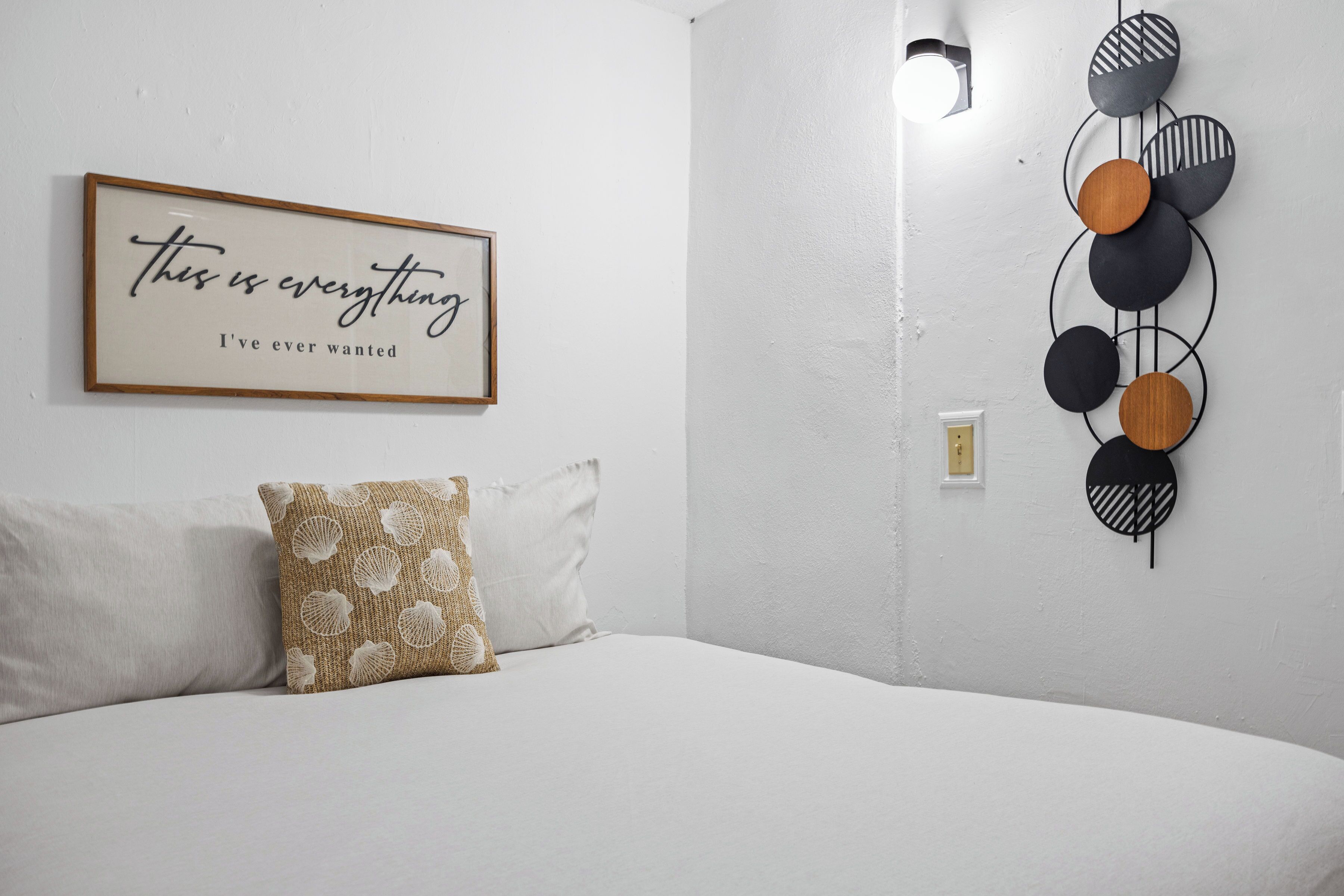 Une chambre à coucher comprenant un lit, une lampe fixée au mur, un cadre avec une citation et un élément décoratif mural.