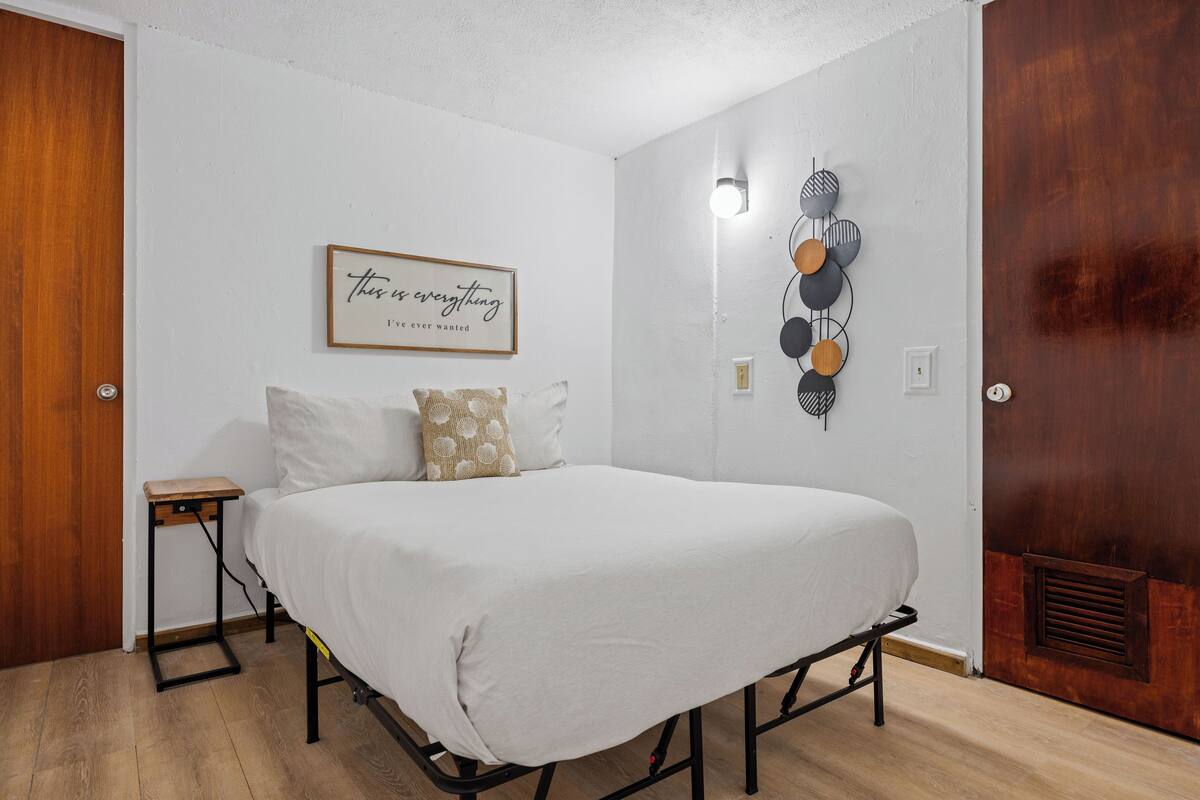 A bedroom with a bed, a bedside table, a wall-mounted light, and a decorative wall piece.