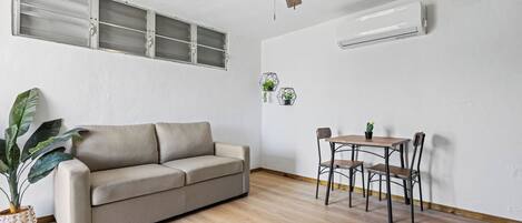 Une pièce comprenant un canapé, une table à manger avec des chaises, un ventilateur de plafond et un appareil de climatisation.