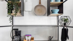 Une petite cuisine équipée d’une machine à café, d’une boîte de biscuits Malanga, d’un panier de biscuits, d’un téléphone intelligent, d’un évier et d’une plante suspendue.