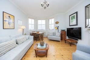A living room with a sofa, a coffee table, a TV, and a dining area with chairs and a table.